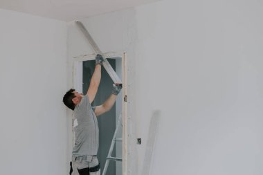 Genç beyaz bir adamın portresi ayakta duruyor ve kapının üstündeki duvara taze macun sergiliyor. Bahar günü geniş ve uzun bir kural koyuyor. Yakın plan, seçici bir odak ile. Çimento ve inşaat işleri kavramı.