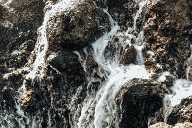 Okyanus suyunun bulanık, köpüklü akıntıları bir sonbahar günü Atlantik Okyanusu 'nun dağlık sahillerindeki doğal bir volkanik havuzda bir kaya oluşumundan süzülüyor. Güzel doğa arka planlarını, volkanik havuzları kavrayın..