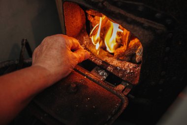 Sol el: Yaşlı, tanınmayan bir kadın, soğuk bir sonbahar gününde banyoda jakuziyi yakmak için odun ateşine kibrit tutuyor. Yan görüntüyü yakından çek. Kavram: Emeklilikte sonbahar yaşam tarzı.