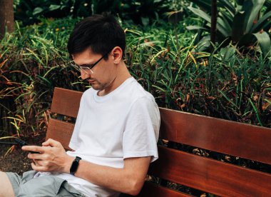 Tenerife 'de bir sonbahar günü etrafı tropik bitki örtüsüyle çevrili bir botanik bahçesindeki bankta oturan koyu saçlı ve akıllı bir beyaz adamın portresi. Kavram: teknolojiyi kullanarak doğada rahatlama.