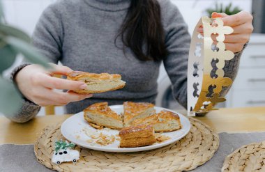 Mutfak masasında oturan beyaz bir kızın portresi. Elinde bir parça kraliyet galeti ve altın bir taç var. Konsept: tatil zamanı, kraliyet galeti yeme zamanı.