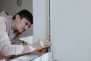 Bir bahar güneşli bir günde plastik bir pencerenin alt köşesinde elleri ile dikkatlice yapıştıran genç ve yakışıklı beyaz bir adamın portresi, sağında fotokopi aletiyle yan görüntü. Tamir konsepti