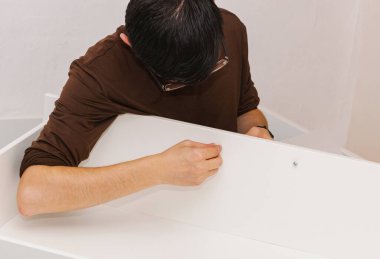 Siyah saçlı, beyaz bir adamın portresi. Geceleri oturma odasında otururken parmaklarıyla vidayı sıkıyor. Orta ölçekli bir yan görüş..