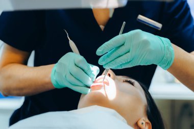Tanımlanamayan, yeşil lateks eldivenli beyaz bir dişçi, özel bir klinikte diş aletleri kullanan genç bir kızın ağız boşluğundaki alt çenesindeki tartarı temizler. Tedavi kavramı