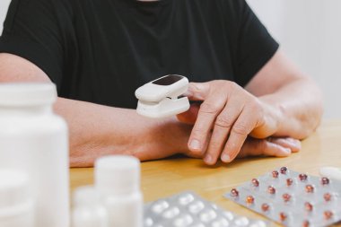Siyah tişörtlü, tanınmayan yaşlı bir kadının portresi tek başına nabzı ölçüyor. Tahta masada oturuyor, gündüz vakti haplar odada, çok yakından bakıyor. Teknoloji kullanım süresi kavramı, emeklilik
