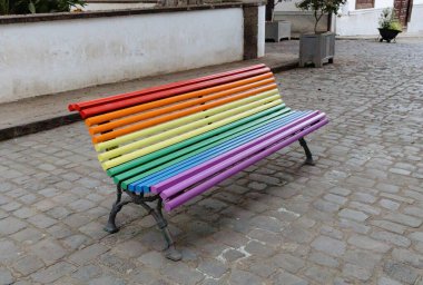 Gökkuşağı renkli ahşap bir bankın güzel yatay görüntüsü bir sonbahar günü bir ada caddesine kurulmuş, yan görünüş, orta çekim. Gökkuşağı şehir sanatı konsepti.