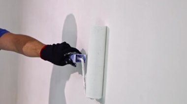 Kafkasyalı tanınmayan bir gencin eli, bir rulo ve beyazla resim yapıyor. Oturma odasının duvarını boyuyor. Yaz günü ferahlatıcı bir yenileme yapılıyor.