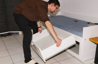 Siyah saçlı, beyaz bir çenesi olan beyaz bir adamın portresi beyaz bir yatağın içine çekmeceyi sokmaya başlıyor, akşam salonda toplandıktan sonra kontrol ediyor, orta ölçekli. Yatak kurulumu kavramını, adım adım talimatları.