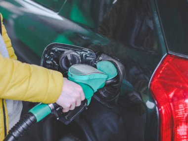 Sarı ceketli genç beyaz bir adamın elinde bir benzin istasyonu silahı var ve bir benzin deposuna benzin dolduruyor. Kenar manzaralı bir benzin istasyonunda. Benzin istasyonu konsepti, servis.