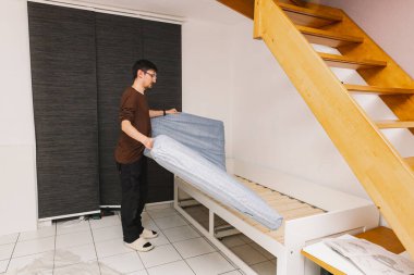 Kafkasyalı genç bir işçi, akşam merdivenlerin altındaki odada, üst ranzanın üzerine yeni bir gri-mavi yatak yerleştiriyor. Yatak kurulumu kavramı.