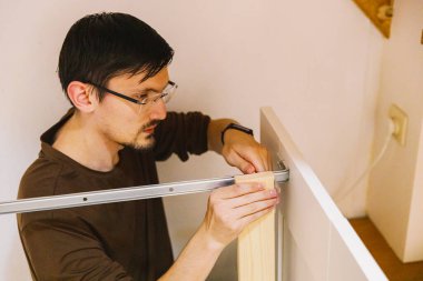 Genç, yakışıklı, beyaz bir işçi manuel olarak vidayı bir deliğe vidalayarak bir odada yatak monte ederken metal bir vidaya bağlıyor. Yakın plan, yan görüş. Kavramsal yatak montajı.