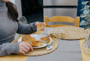 Tanınmayan beyaz bir kız, ahşap bir masada, mutfakta tek başına oturuyor ve elinde kraliyet galetesinden bir parça tutuyor, yukarıdan yakın çekim manzarası. Konsept: tatil zamanı, kraliyet galeti yeme zamanı.