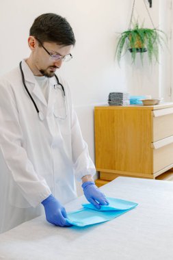 Yakışıklı genç beyaz bir adam randevusundan önce çalışma alanını hazırlıyor, bir klinikteki masada dururken emici pedi açıyor. Yan görüş, yakın çekim. Evcil hayvanlar için sağlıklı yaşam tarzı kavramı.