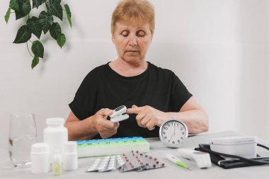 Son sınıf güzel bir kadının portresi, parmaklarıyla nabzını ölçen bir aletle masada oturan haplar ve çalar saatle gündüz vakti odada, yan görüş yakın. Teknoloji ve emeklilik yaşam tarzı kullanma zamanı kavramı.