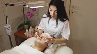 Genç, güzel bir doktor kız kozmetik uzmanı, tıbbi köpük ve masaj hareketleriyle bir müşterinin yanaklarını ve çenesini temizler. Güzellik salonundaki masaj masasına gözlerini kapatmış, yakından bakar. Terapötik yüz bakımı