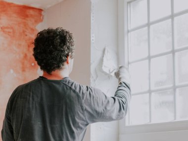 Beyaz, genç bir adam gri tişörtlü, kolları kıvırcık, kahverengi saçlı bir alçı, pencere aralığında küçük bir spatula ile yeni macunu dengeliyor. Dairelerin ve evlerin tamiri, duvarların sıvanması.