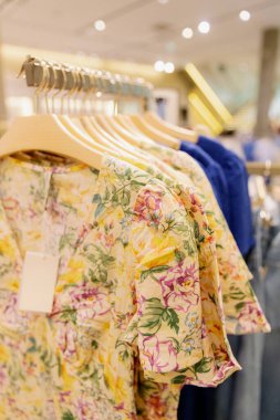 Alışveriş merkezindeki askıda asılı renkli çiçek desenli kısa kollu elbisenin güzel manzarası, seçici bir odak ile yan manzara. Alışveriş zamanı kavramı, kadın giyimi.