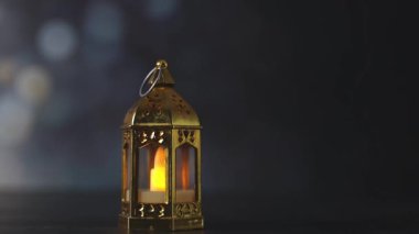 Bulanık bir bokeh ile karanlık bir taş arka plan, küçük yaldızlı bir Fas kule feneri, bir LED mum standı, yandan çekim, yavaş çekim yakın çekim ve sağ iz. Şenlikli dekor konsepti, Ramazan Kareem.