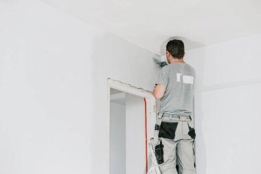 Gri üniformalı yakışıklı beyaz bir adam ve merdiven üzerinde duran eldivenler akşamları kapısında spatula bulunan bir kapı aralığını kaplıyor ve bina feneri açık ve yakın çekim alanı kopyalıyor. İnşaat konsepti.