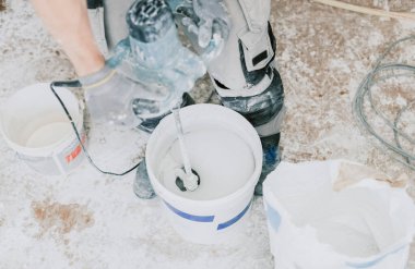 Tanımlanamayan beyaz üniformalı genç bir adam odada duruyor ve beyaz ıslak macunu kovayla karıştırıcı ile kırbaçlıyor. Üst tarafı seçici odaklı. Ev yenileme konsepti, inşaat işi.