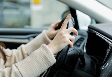 Tanınmayan, bej kazak giyen beyaz bir kadın ellerini direksiyonun üzerine koyup işaret parmağını kaldırarak arabada oturuyor. Yan görüntüyü yakından çek. Kavram: Güvenli sürüş ve eğitim.