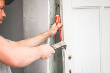 Olgun, deneyimli bir Kafkasyalı çilingir eski ahşap bir kapıdan levye ve tornavidayla mors kilidini çıkarır. Yan görüntüyü yakından çek. Konsept: Tamir işi, kapı kilidi değiştirme ve yenileme.