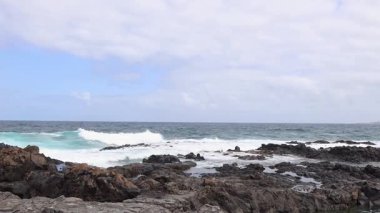 Tenerife adasındaki bulutlu bir sonbahar gününde Atlantik Okyanusu 'ndaki volkanik kayalık bir sahil şeridine yuvarlanan güçlü, köpüklü dalgaların görüntüsü, orta yüksek çekim, yavaş çekim. Güzel deniz arka planlarını kavra.
