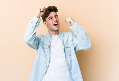 Beyazlı genç adam bej arka planda izole edilmiş zafer kazandıktan sonra yumruğunu kaldırıyor, kazanan konsept.