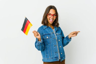 Beyaz arka planda izole edilmiş bir Alman bayrağı tutan genç Latin kadın işaret parmaklarıyla işaret ederek heyecanlanıyor..