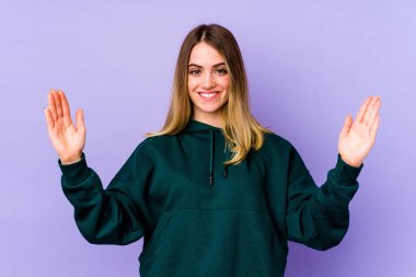 Mor arka planda izole edilmiş beyaz bir kadın. Elinde parmakları olan, gülümseyen ve kendinden emin bir şey tutuyor..