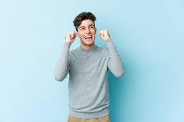 Mavi arka planda izole edilmiş genç beyaz bir adam zaferden sonra yumruğunu kaldırıyor, kazanan konsept..