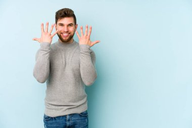 Mavi arka planda izole edilmiş genç beyaz adam on numarayı elleriyle gösteriyor..