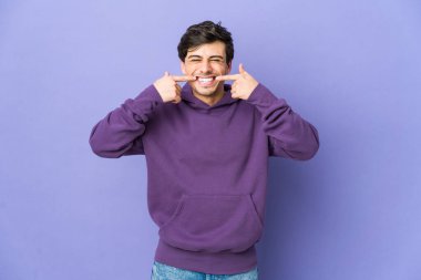 Genç havalı adam gülümsüyor, parmaklarıyla ağzını işaret ediyor..