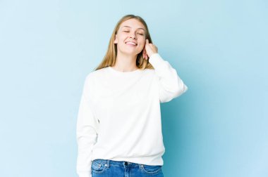 Mavi arka planda izole edilmiş genç sarışın kadın zaferi, tutkuyu ve coşkuyu kutluyor, mutlu bir ifade..