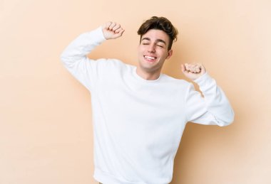 Beyazlı genç adam bej arka planda izole edilmiş özel bir günü kutluyor, atlıyor ve enerjiyle kollarını kaldırıyor..