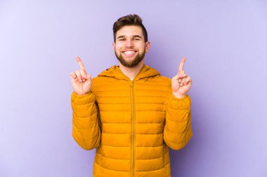 Mor arka planda izole genç adam iki ön parmağı da boş bir alan gösteriyor..