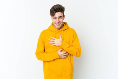 Beyaz arka planda izole genç beyaz adam mutlu bir şekilde gülüyor ve ellerini karnının üstünde tutarak eğleniyor..