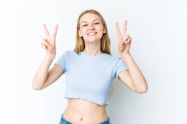 Beyaz arka planda izole edilmiş genç sarışın kadın zafer işareti gösteriyor ve gülümsüyor..