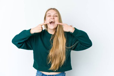 Beyaz arka planda izole edilmiş genç sarışın kadın gülümsüyor, parmaklarını ağzına doğrultuyor..
