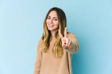 Mavi arka planda izole edilmiş genç beyaz kadın iki numarayı parmaklarıyla gösteriyor..