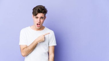 Mor arka planda izole edilmiş genç beyaz adam yan tarafı işaret ediyor.