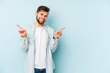 Mavi arka planda izole edilmiş genç beyaz adam farklı kopya alanlarını gösteriyor, birini seçiyor, parmaklarıyla gösteriyor.