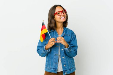 Beyaz arka planda izole edilmiş bir Alman bayrağı tutan genç Latin kadın gülümsüyor ve elleriyle kalp şeklini gösteriyor..