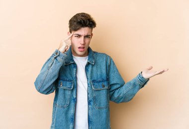 Beyazlı genç bir adam bej arka planda izole edilmiş ve elinde bir ürün var..