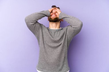 Mor arka planda izole edilmiş genç beyaz adam, mutlu bir şekilde ellerini başının üstünde tutarak gülüyor. Mutluluk kavramı.