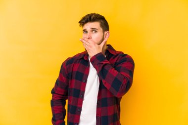 Sarı arka planda izole edilmiş genç beyaz adam elleri endişeli bir şekilde ağzı örtüyor..
