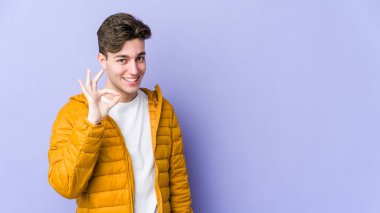 Genç beyaz adam mor arka planda izole edilmiş neşeli ve kendinden emin, iyi bir jest yapıyor..