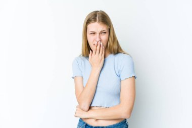 Beyaz arka planda izole edilmiş genç sarışın kadın esniyor. Ağzı eliyle kapatan yorgun bir hareket sergiliyor..