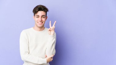Mor arka planda izole edilmiş genç beyaz adam iki numarayı parmaklarıyla gösteriyor..