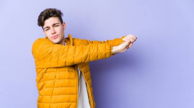 Mor arka planda izole edilmiş genç beyaz adam kollarını uzatıyor, rahat pozisyonda..